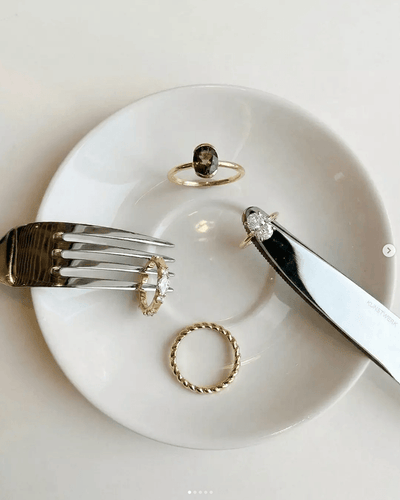 Four gold rings displayed on white plate with cutlery, featuring oval smoky quartz, diamond halo, twist band, and solitaire styles