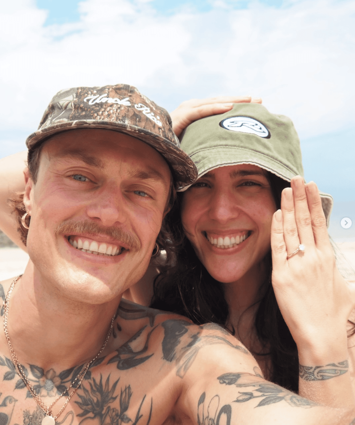 Engaged couple smiling at the beach with diamond ring