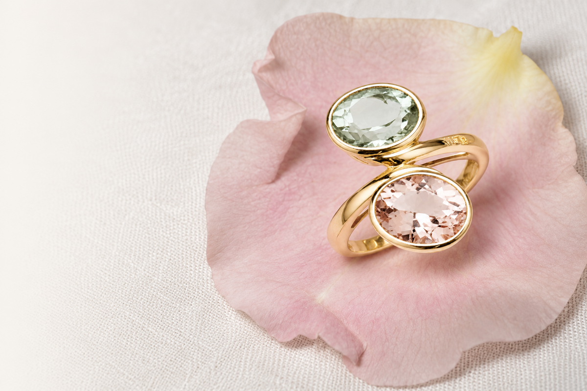 A green and blush two-stone ring on a pale pink petal and ivory linen.