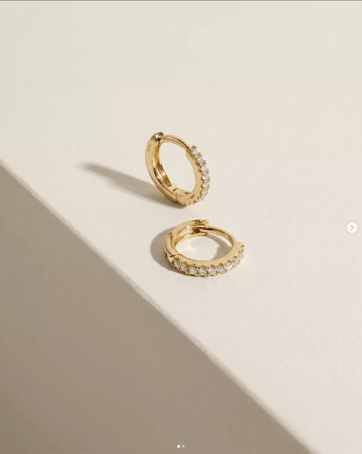 Gold diamond huggie earrings on a cream jewellery display